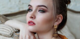 Czy makijaż może poprawić twój nastrój? Tak! Kobieta na zdjęciu wpatruje się w dal, siedzi oparta o sofę. NA twarzy ma subtelny makijaż.