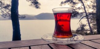 Herbata czerwona to utlenione liście herbaty chińskiej lub krzewu o nazwie rooibos. Oba napary mają bardzo intensywną czerwoną barwę i lekko karmelowy posmak. Na zdjęciu w szklance ukazany charakterystyczny kolor czerwonej herbaty na tle jeziora.